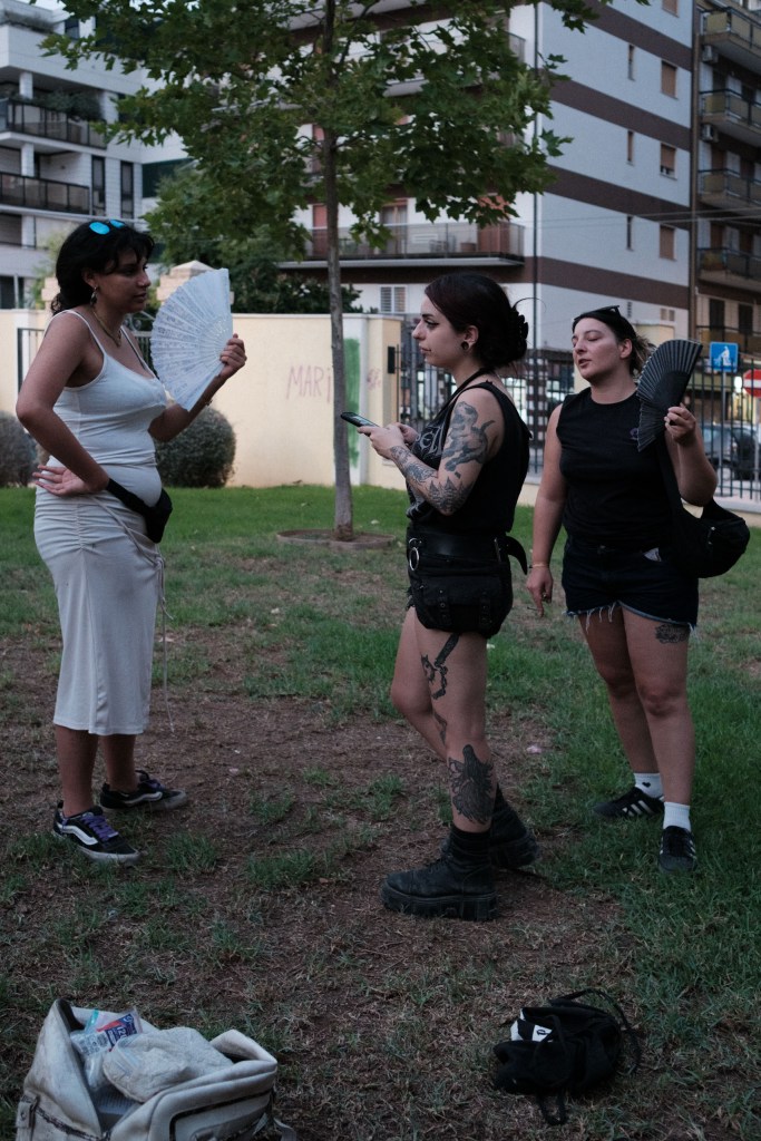 Three women holding folding fans against the evening heat, apartment buildings behind them.
