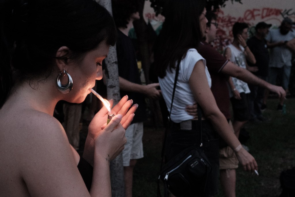 Close-up of a hand cupping a lighter flame to light a cigarette at dusk.