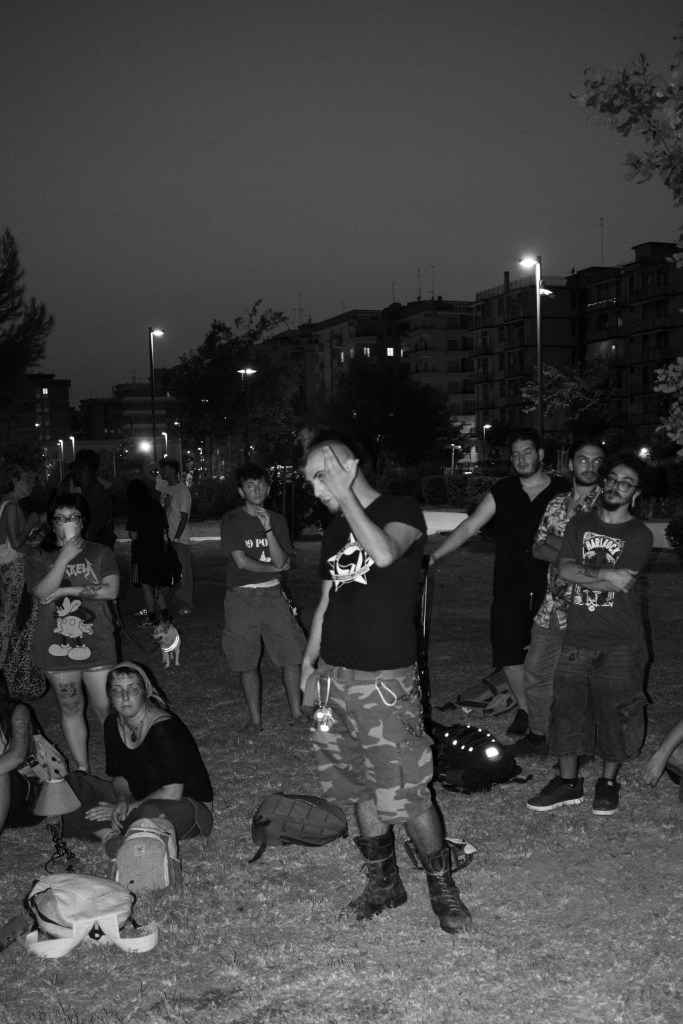 A nighttime crowd standing in a park, streetlights and apartment blocks in the background.