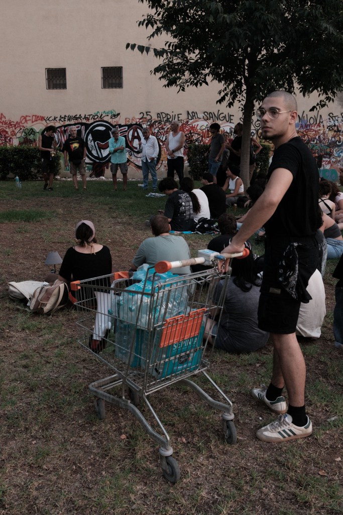 A man pushing a shopping cart loaded with water bottles through a crowd at a public assembly.
