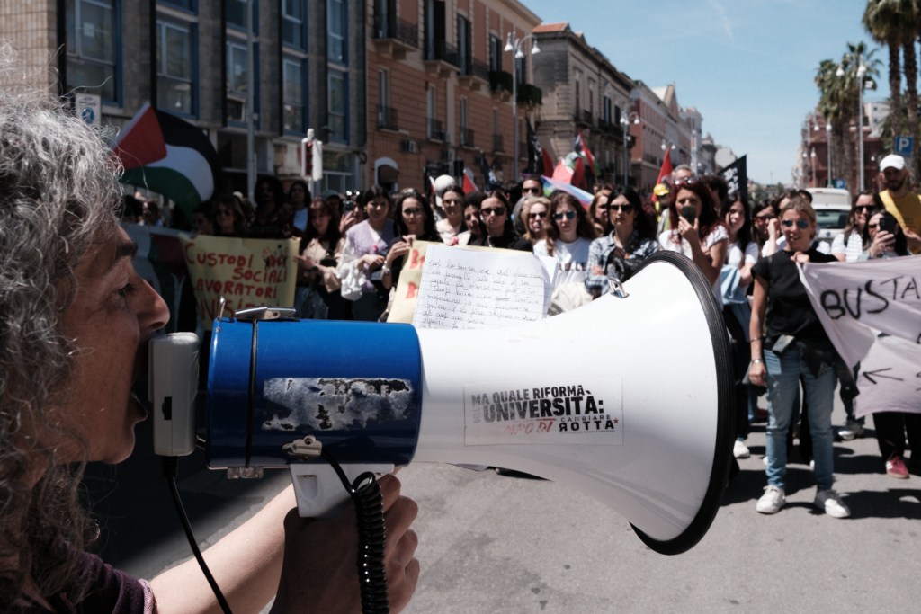 A woman speaks through a megaphone to the crowd, handwritten notes tucked into the speaker.