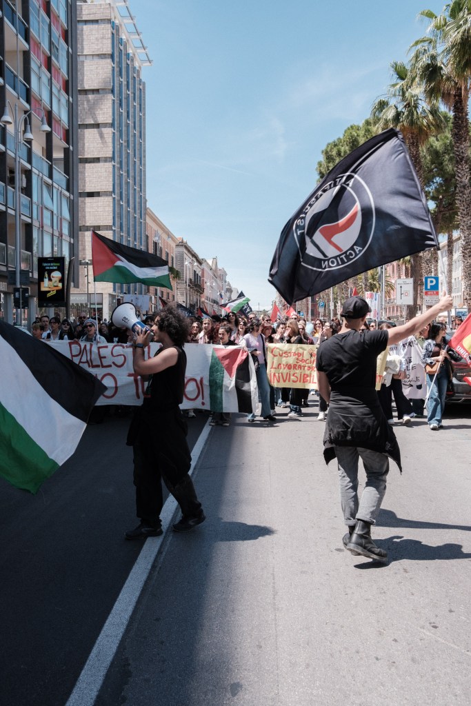 The march seen from behind, an antifascist flag in the wind, union and Palestine banners side by side.