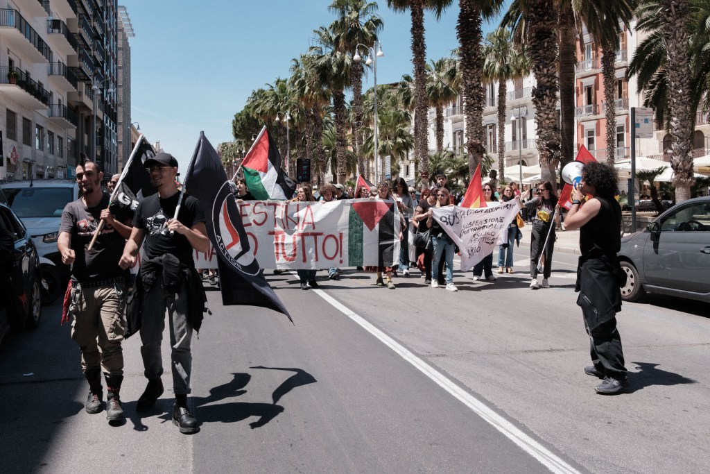 Antifascist and Palestinian flags fly over the march, banners about suspended wages behind them.