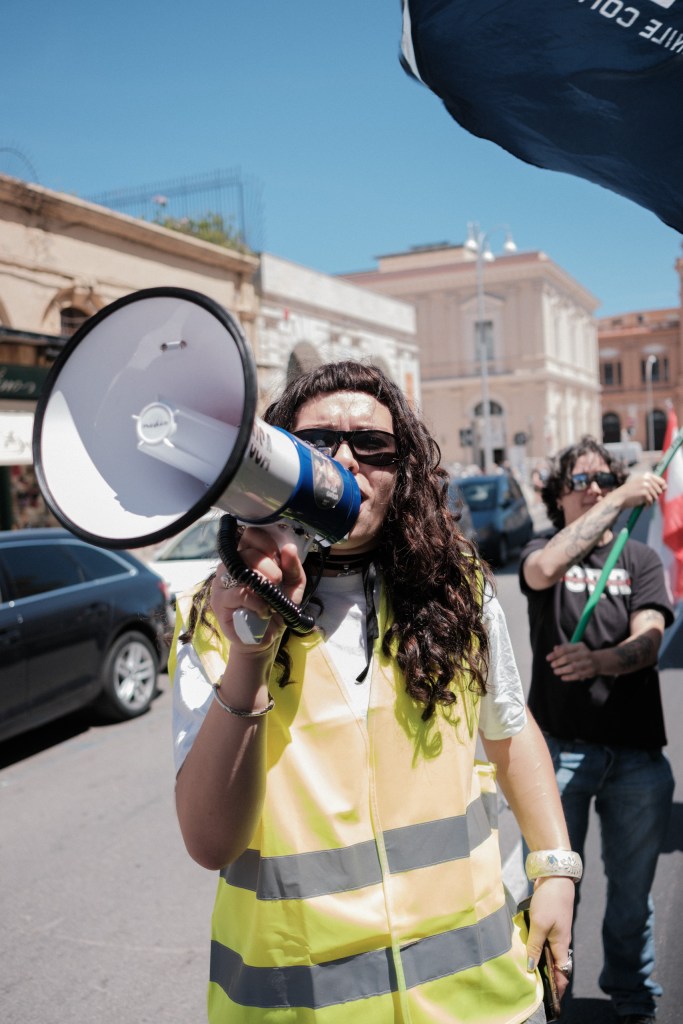 A marcher shouts into a megaphone, sunglasses on, another marcher with a Lebanese flag behind her.