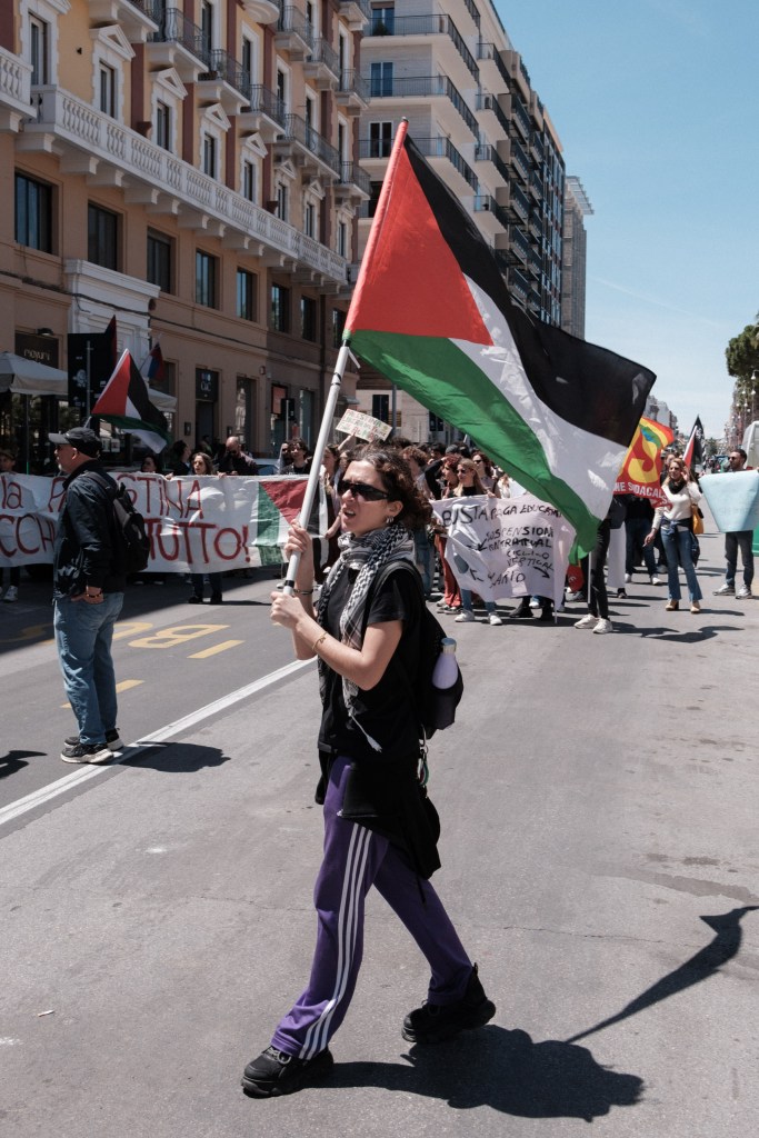 A marcher carries a Palestinian flag down the street, the march behind her.