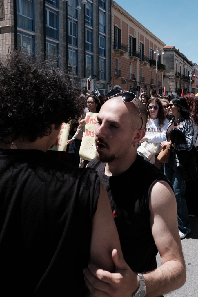 Two marchers speak closely, a "more dignity" sign visible in the crowd.