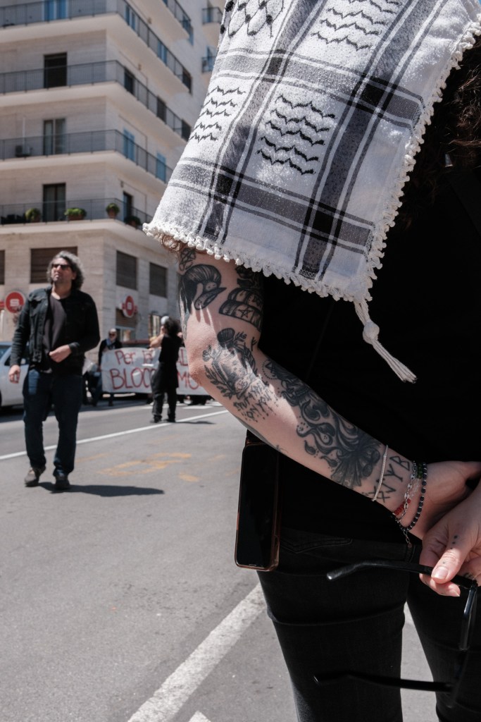 A tattooed arm rests a keffiyeh on another marcher's shoulder, the march behind them.