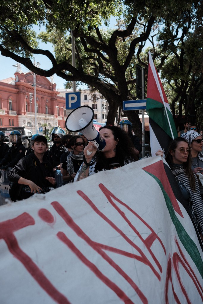 A marcher with a keffiyeh around her neck shouts into a megaphone in front of the police line.
