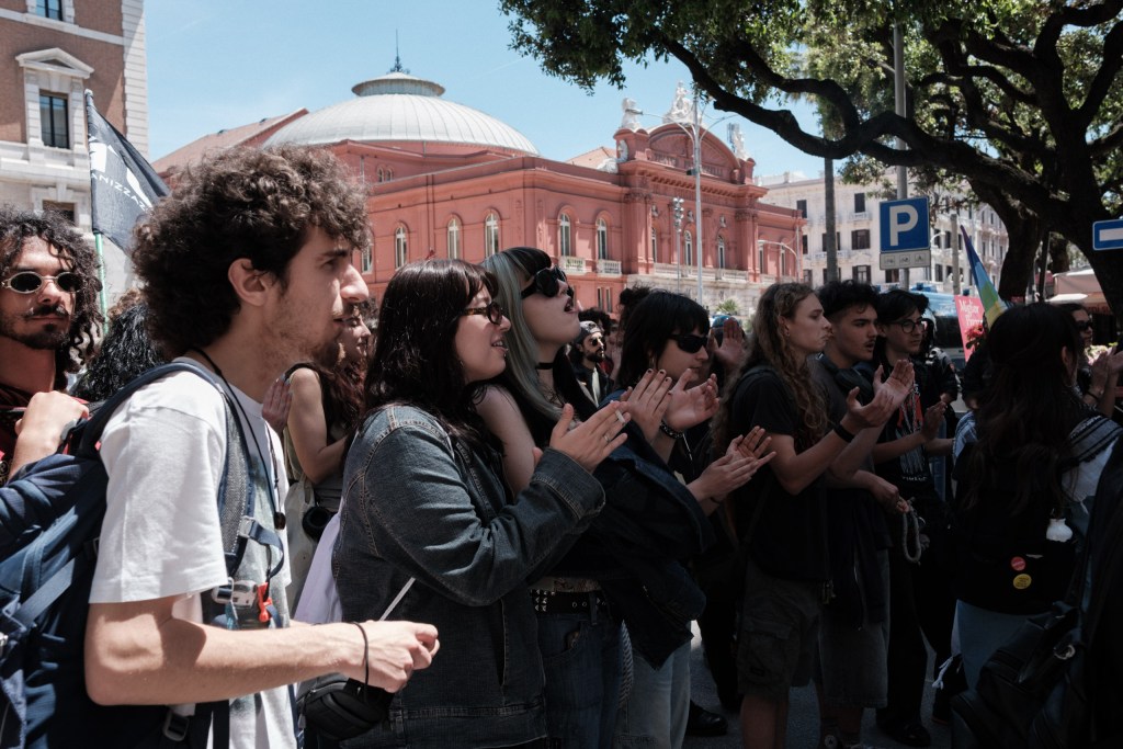 Marchers applaud, the dome of Teatro Petruzzelli visible through the trees, Bari.