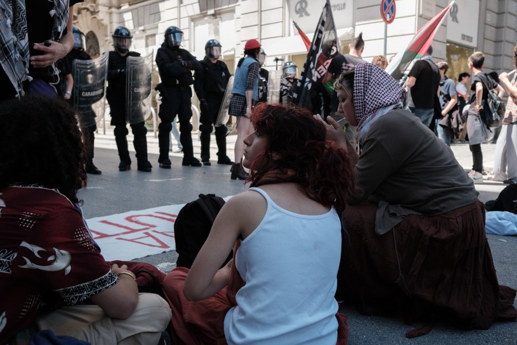 Two marchers sit on the ground near the police line, waiting during the standoff on Via Calefati.