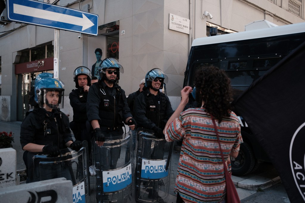 Officers with "Polizia" shields in front of a Carabinieri van, warm late-day light, Via Calefati.