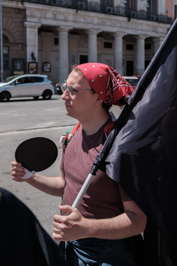 Marcher in a red bandana with a black flag over his shoulder looks out over the square by Bari's Prefettura.