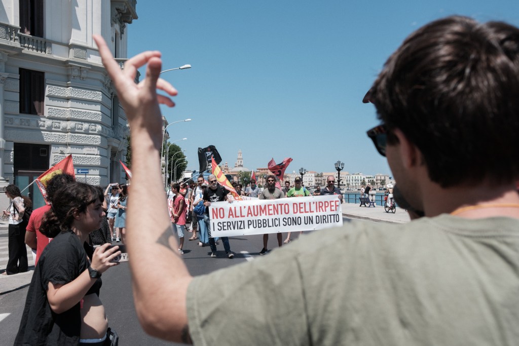 Marcher raises a hand in front of the anti-IRPEF banner on Bari's seafront.