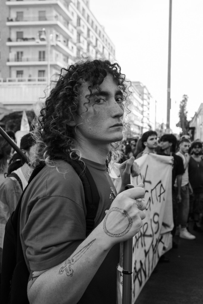 Curly-haired young protester looks over his shoulder, a serpent tattoo on the hand holding his flagpole.