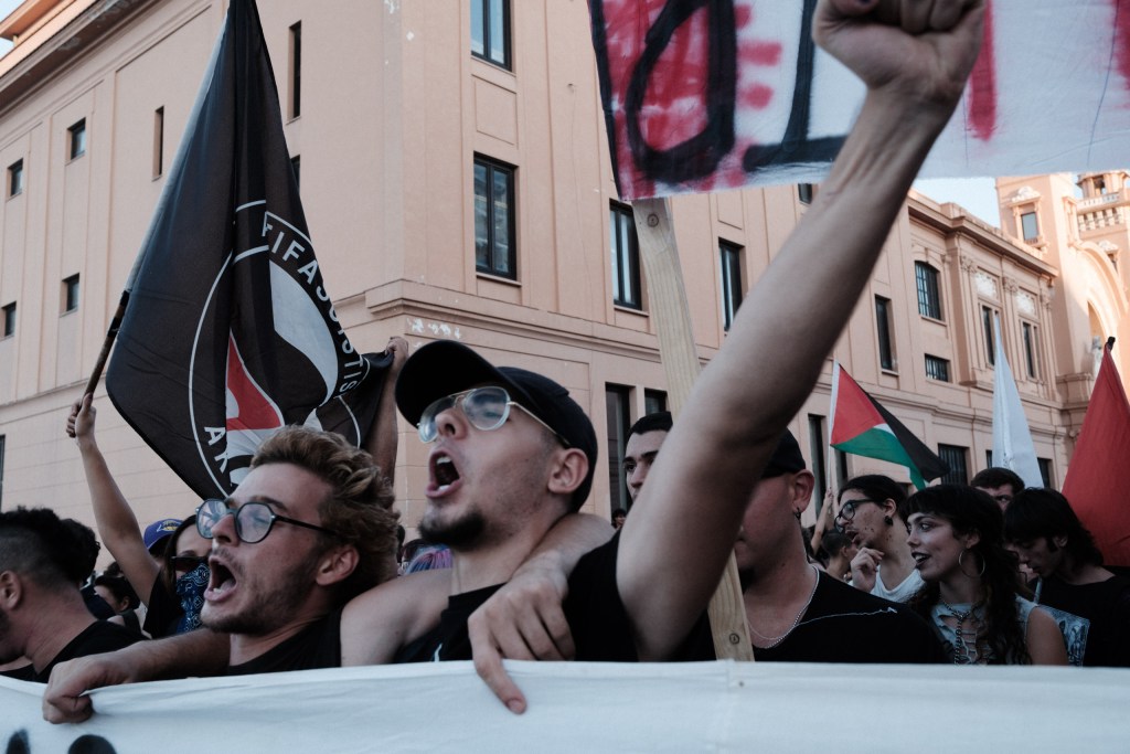 Young men chant behind the front banner under antifascist and Palestinian flags.
