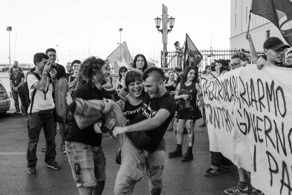 Two protesters carry a laughing woman in their arms while the crowd around them smiles.