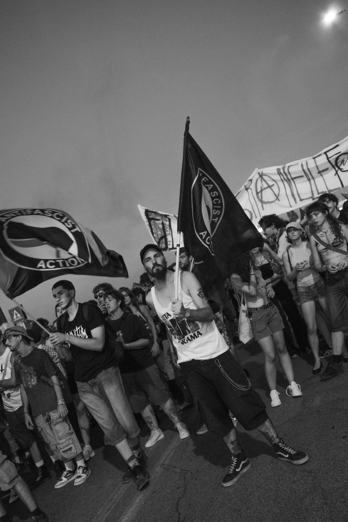 Bearded protester waves an Antifascist Action flag among young marchers in the evening.