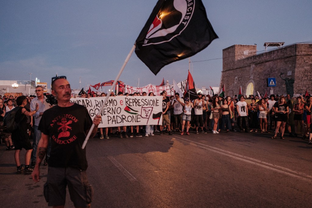 Man waves an antifascist flag in front of the stopped march on the Bari seafront.