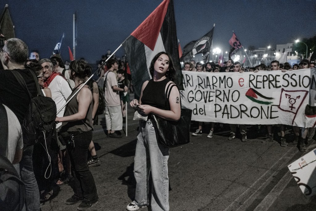 Young woman stands in the middle of the road at night next to a Palestinian flag.