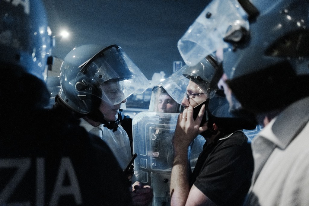 Helmeted officers confer behind their shields, one talking on the phone.